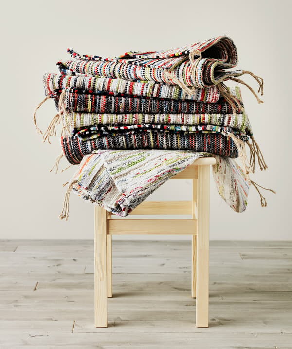 Several colourful TÅNUM rugs stacked on a small stool.