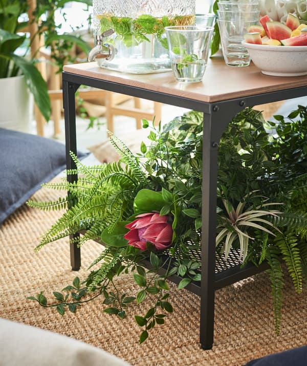 Several IKEA FEJKA artificial potted plants on the bottom shelf of a table.
