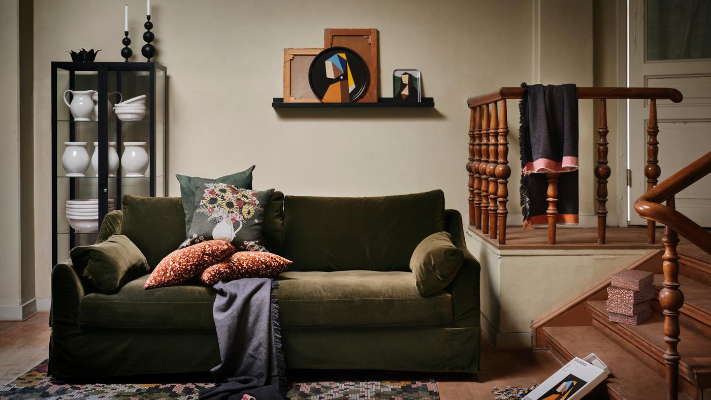 Several items from the IKEA DEKORERA collection stand in a warm living room, with a dark green sofa with cushions.
