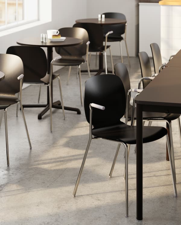 Several large tables with matching chairs and next to it several small round tables with chairs, a white mug and a window.