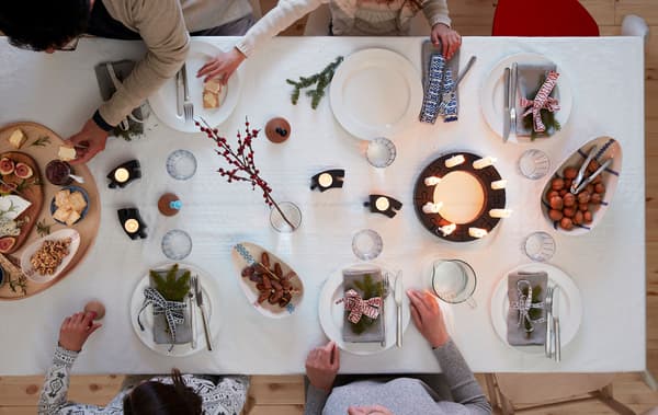 Several persons seated around a table set for a festive occasion: napkins, decorations, lit LED candles, cheese platter.