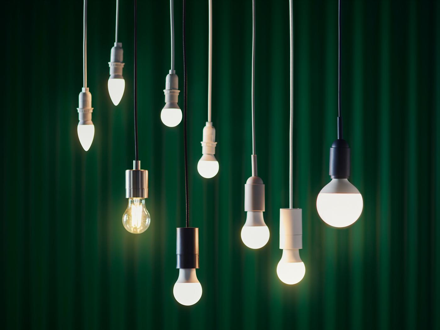 Several SOLHETTA bulbs of different sizes and shapes are hanging from the ceiling in front of a dark green background.