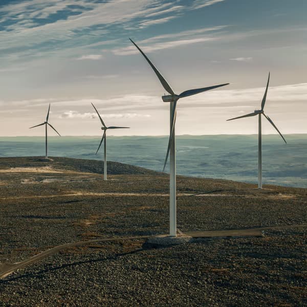 Several wind turbines stand tall on a hilly landscape, harnessing the power of the wind under a cloudy sky.