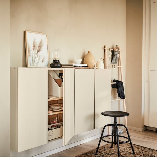 Several wooden IKEA IVAR cabinets on a wall with decorative accessories on top and a black stool in the foreground.