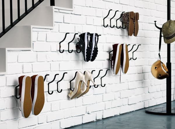 Shoes stored on black hooks mounted on a white brick wall under the stairs in this hall.