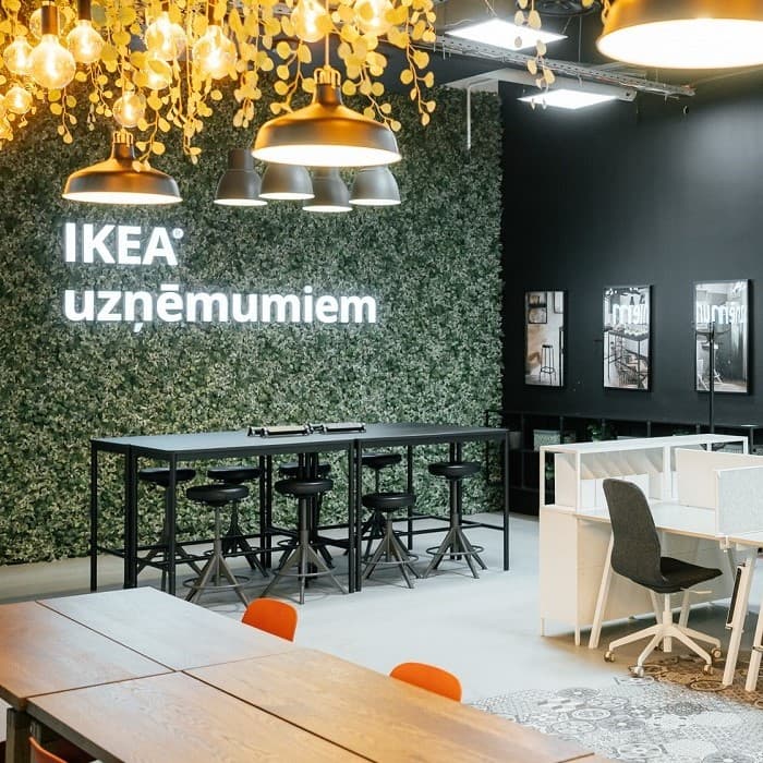 Шоурум IKEA for Business с современным коворкингом, высокими черными столами со стульями, стеной из зелени, стильными подвесными светильниками и эргономичными офисными столами.