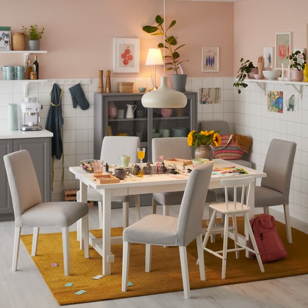 Sillas con funda de la serie BERGMUND, con un comedor con flores y decoración sobre el, lamparas y adornos colgados en el techo.