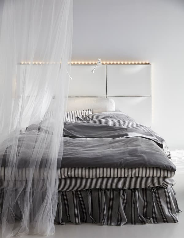 Six white IKEA TRONES shoe cabinets create a headboard for a bed in this white bedroom.