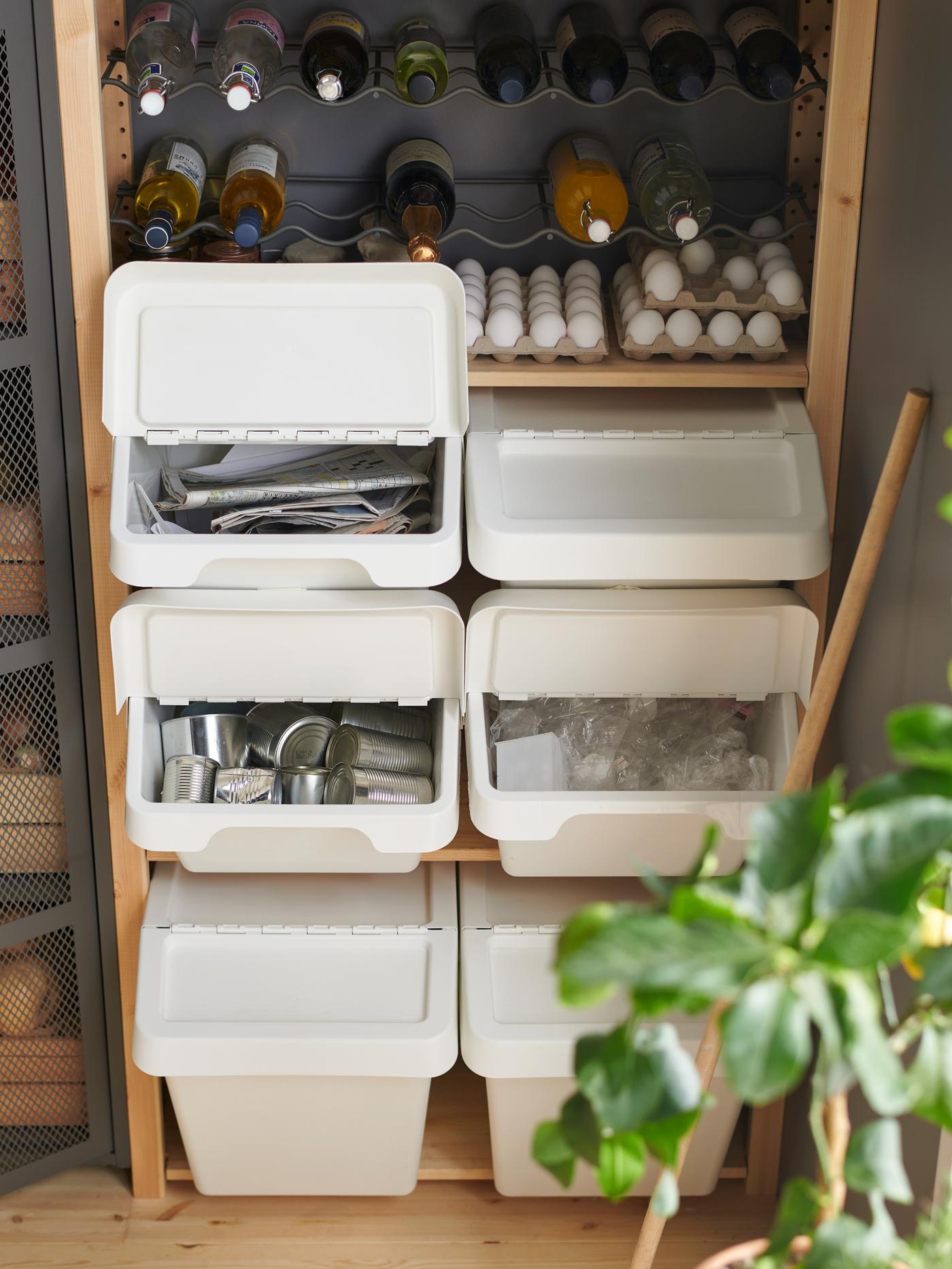 Six white SORTERA waste sorting bins with lid, in two stacks of three, in a wooden shelving unit beneath eggs and bottles.