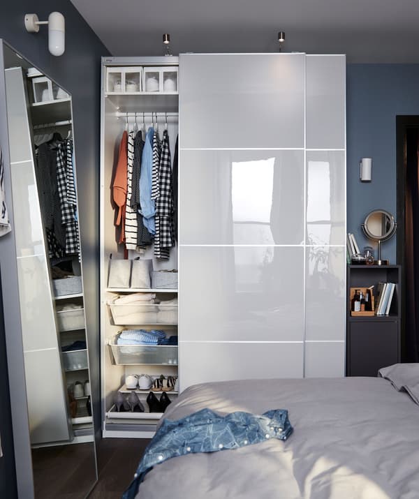 Small bedroom with wall section used in full by a PAX wardrobe, door aside revealing organised content, and a narrow cabinet.