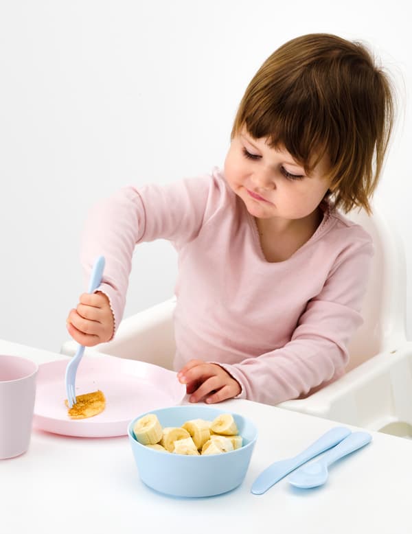 Small girl sitting in a highchair with sliced fruit with blue KALAS tableware.