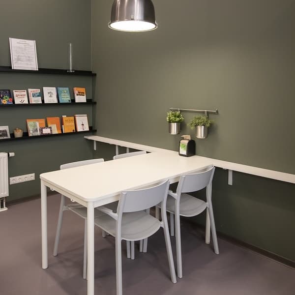 Small office meeting corner with white table, three chairs, green accent wall, and wall-mounted shelves with books.