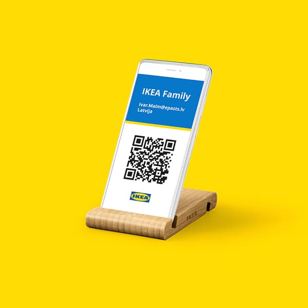 Smartphone displaying an IKEA Family digital membership card with a QR code, placed on a wooden stand against a bright yellow background.