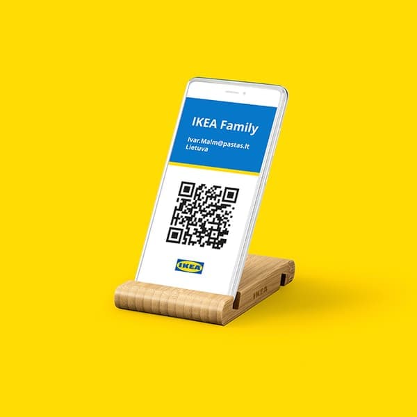 Smartphone displaying an IKEA Family digital membership card with a QR code, placed on a wooden stand against a bright yellow background.