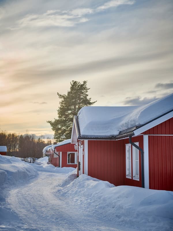 Snötäckt vinterlandskap med röda hus under en molnig himmel vid soluppgång eller solnedgång.