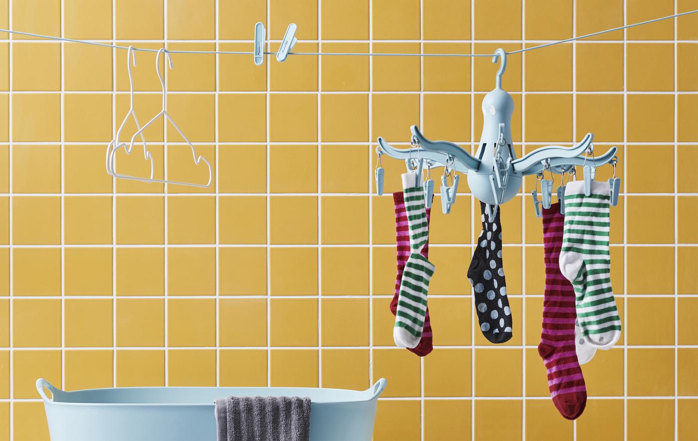 Socks on a blue hanging dryer, pegs and hangers on a clothes line against a wall of yellow tiles.