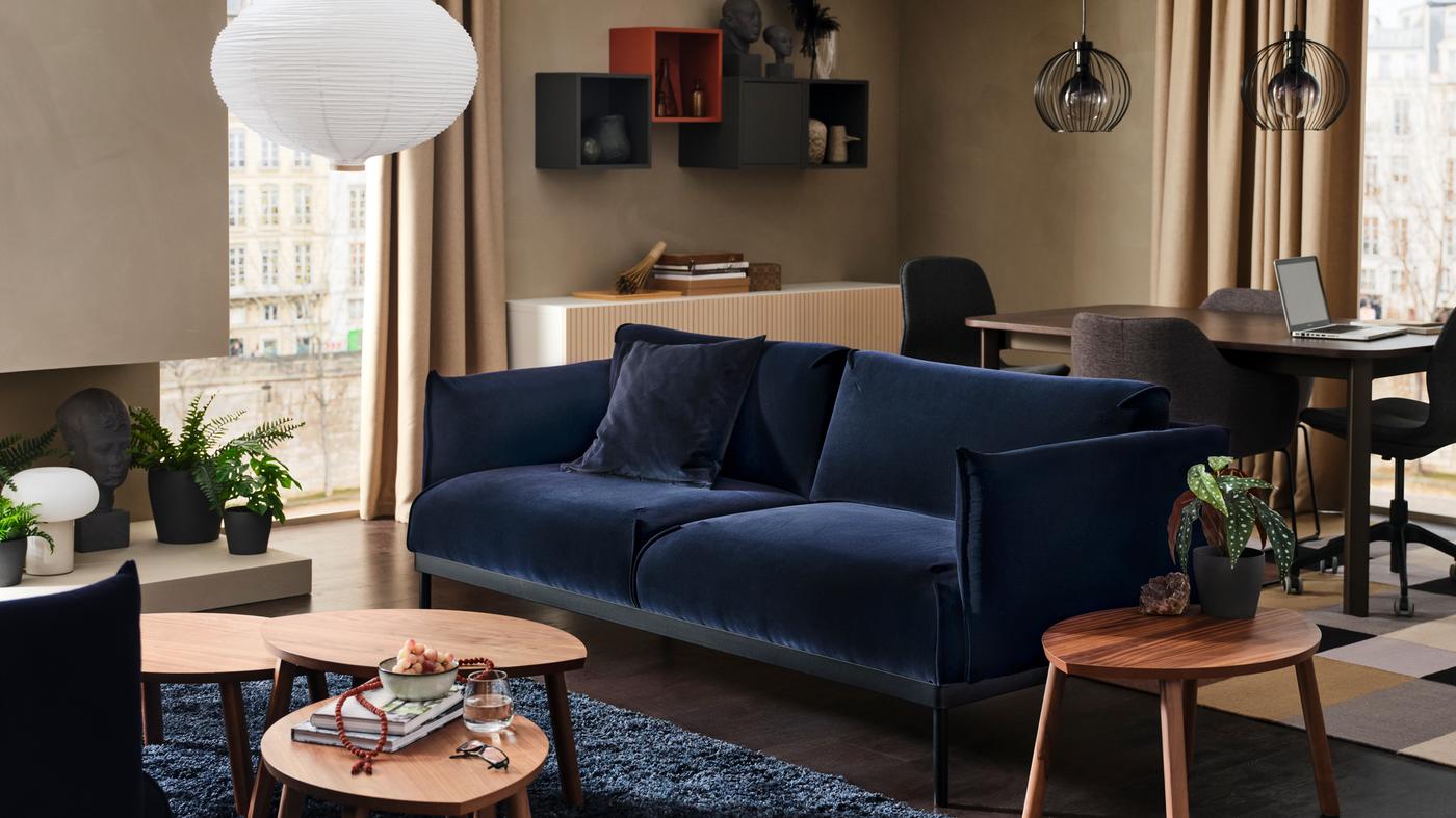 Sofa ÄPPLARYD dengan tiga meja kopi di hadapannya di atas ambal pail tinggi berwarna biru. Meja makan dan kerusi terletak di belakang sofa.