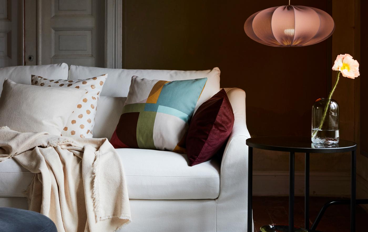 Sofa berwarna putih di ruang tamu dengan kombinasi kusyen dan alas. Di sebelahnya terdapat meja sisi berwarna hitam dan lampu REGNSKUR.