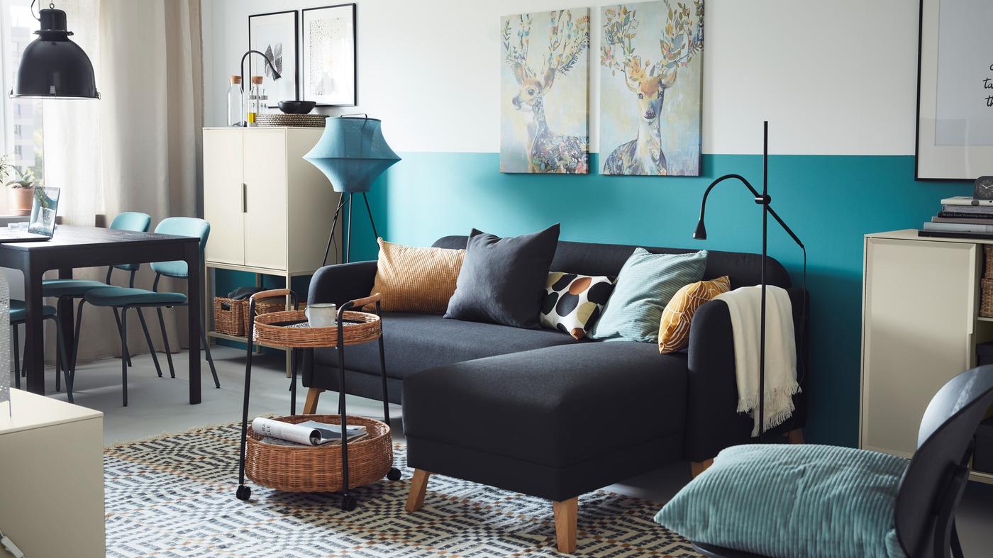 Sofa dengan chaise longue LINANÄS berwarna kelabu gelap di ruang berwarna biru dan kelabu yang cerah dengan troli rotan di hadapannya.