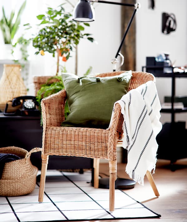 Soggiorno dallo stile grafico in bianco e nero, con elementi in materiali naturali e una poltrona AGEN in rattan con cuscino verde.