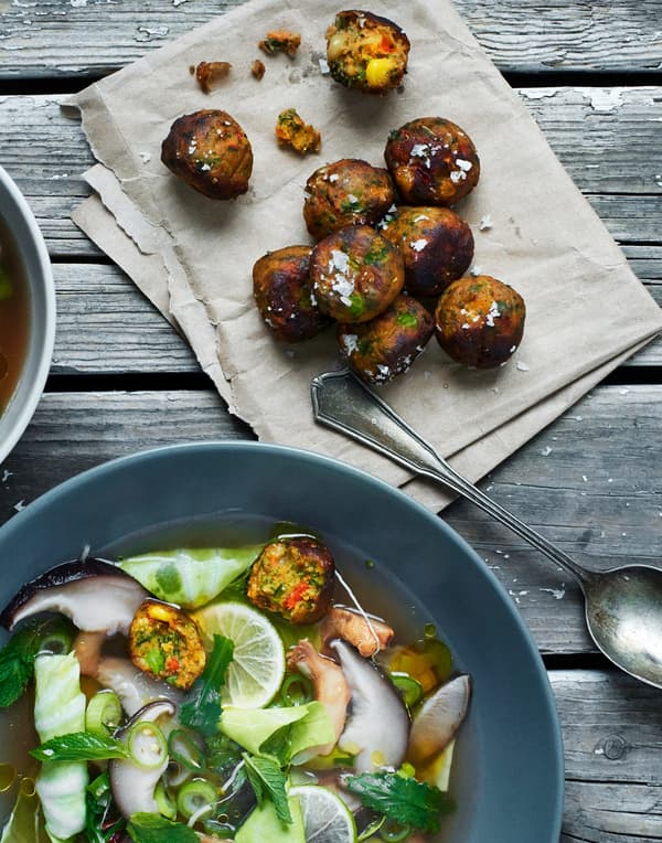 Some fried plant-based veggie balls lying beside a soup bowl with lots of greens and some veggie balls in it.