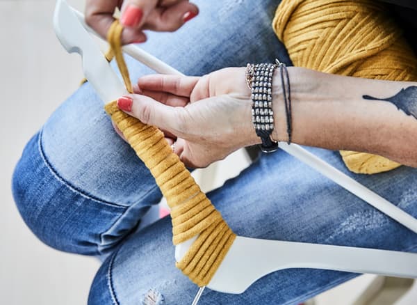 Someone wrapping thick, yellow string around a white BUMERANG hanger to create a unique decorative element.