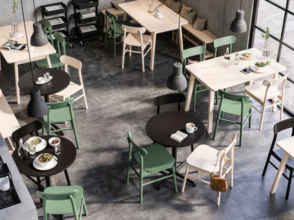 Square and round tables in a café space, all with RÖNNINGE chairs. Large HEKTAR pendant lamps hang from the ceiling.