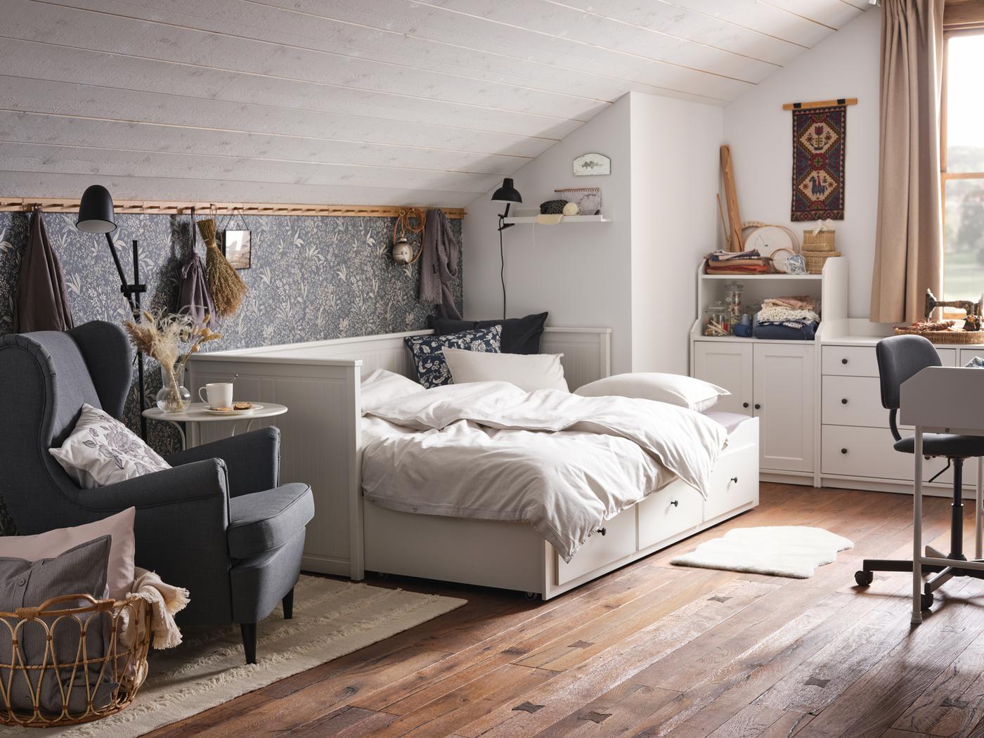 سرير نهاري مع 3 أدراج HEMNES أبيض في غرفة علوية على الطراز الريفي بأرضية خشبية. وبجانبها يوجد كرسي بذراعين STRANDMON.