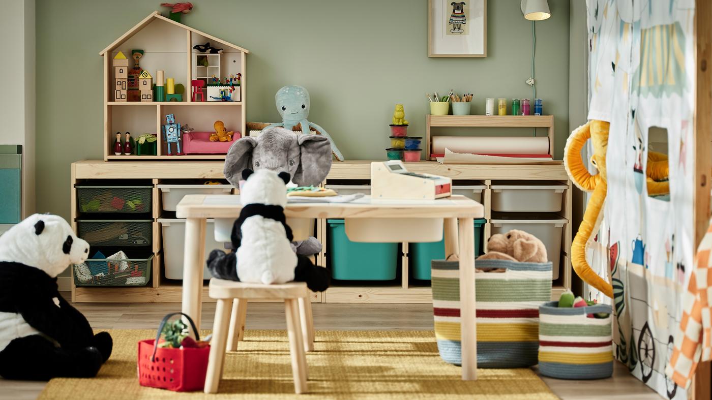 Stofftiere sitzen rund um einen Kindertisch mit Hockern. Im Hintergrund sind Gestelle mit Spielzeugaufbewahrungen zu sehen.