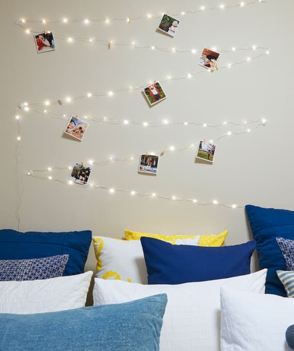 String lights and photos zig-zagged on the wall above a bed filled with cushions.