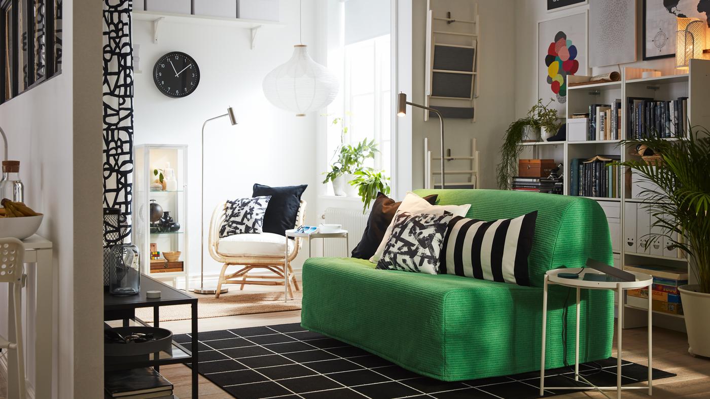 Studio kecil dengan katil sofa 2 tempat duduk berwarna Vansbro hijau terang, tekstil berwarna hitam dan putih, rak buku berwarna putih, kerusi berlengan.