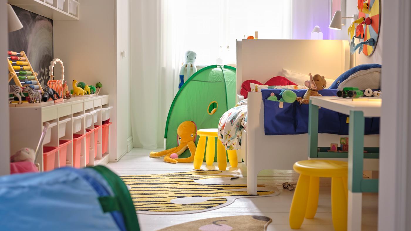 Su un lato di una cameretta, un letto allungabile BUSUNGE con accanto uno sgabello MAMMUT giallo e una tenda da gioco verde dietro.