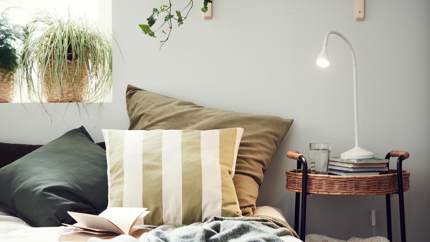 Su un letto vicino a una finestra si vedono dei cuscini con fodere diverse, tra cui la fodera a righe HILDAMARIA – IKEA.