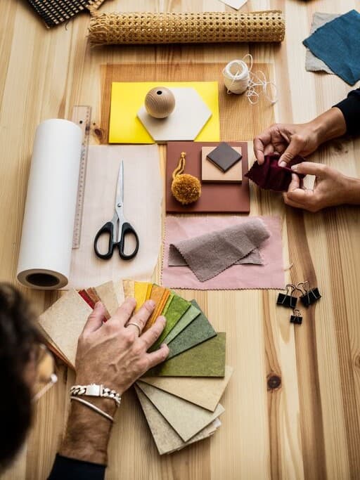 Su un tavolo ci sono diversi campioni di tessuto e cartelle colori per la progettazione di una stanza.
