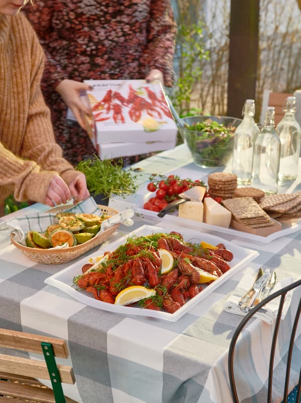 Sunlit table being set for a party, with a heap of KRÄFTOR crayfish on one SMULA tray, cheese and crackers on another.