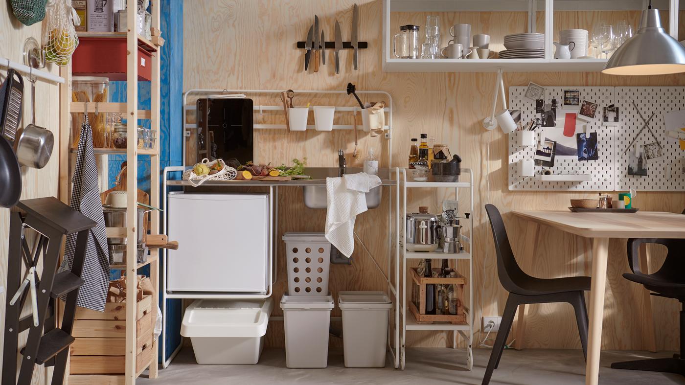 SUNNERSTA kitchenette with accessories, an IVAR shelving unit and a table and chairs in a small room with plywood walls.