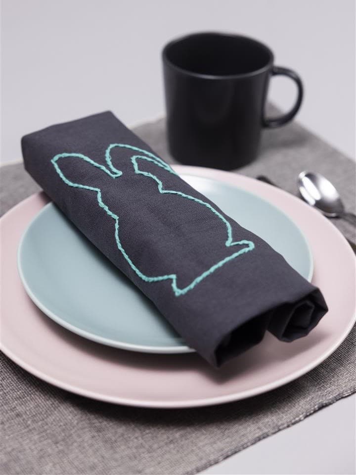 Sur une assiette bleue, il y a une serviette avec un lapin dessus et une tasse noire dans le coin supérieur droit.