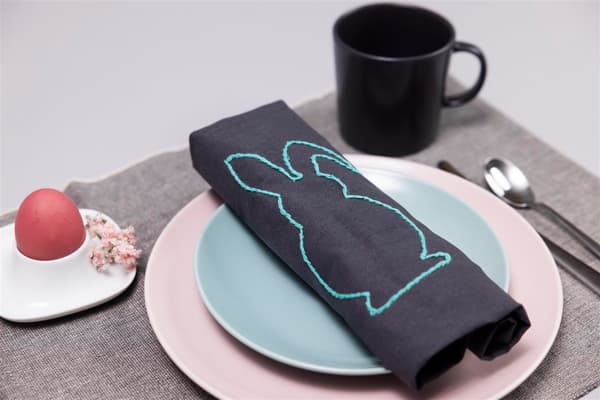 Sur une assiette bleue se trouve une serviette avec un lapin dessus et une schwarzen Tasse oben rechts in der Ecke.