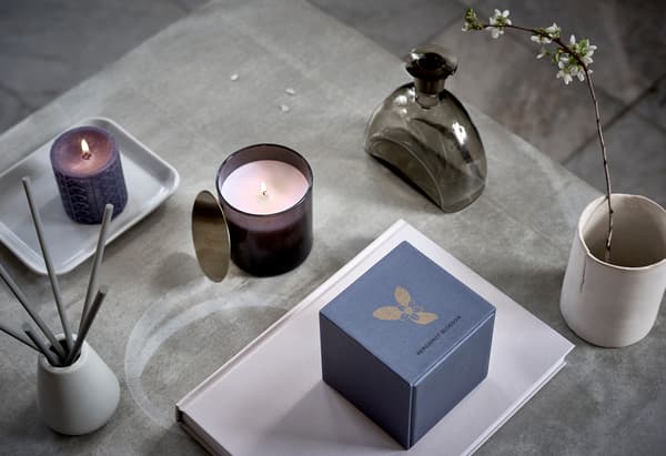 Surface with symmetric arrangement of scented candles, a cup with a twig in bloom, and similar spa-style decorations.