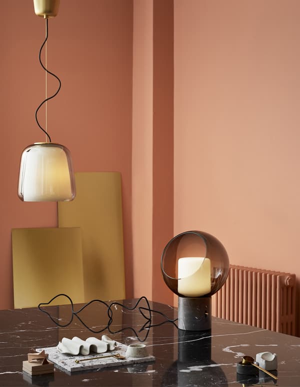 Suspension et lampe de table dans une pièce rose avec table en marbre noir.