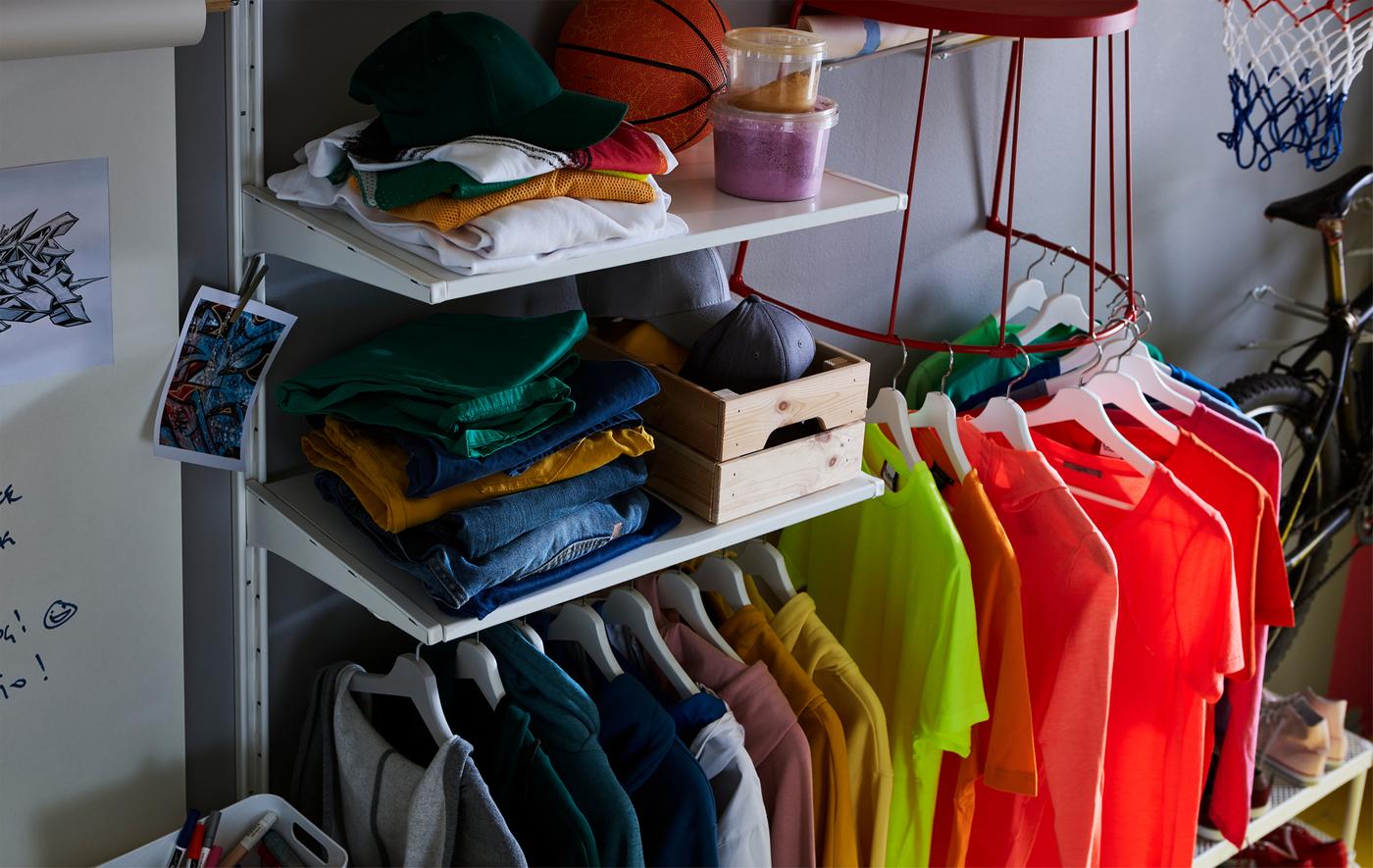 T-shirts sur cintres, accrochés à la structure en acier d’un tabouret IKEA TRANARÖ fixé au mur.