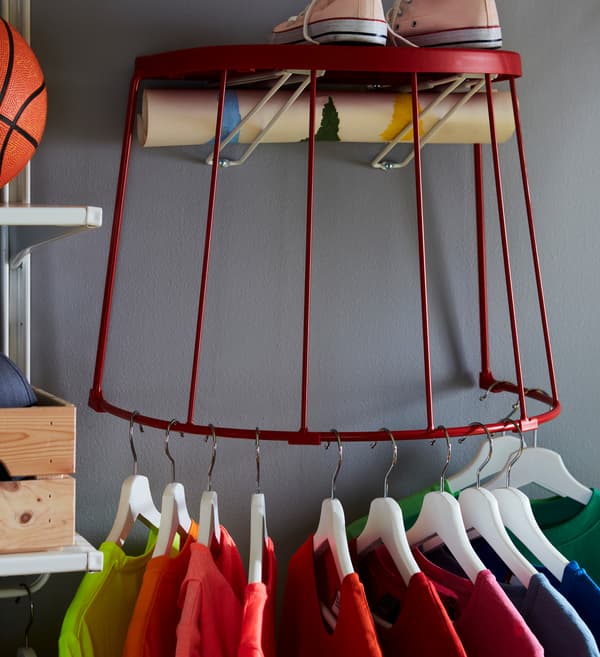 T-shirts sur cintres, accrochés à la structure en acier d’un tabouret IKEA TRANARÖ fixé au mur.