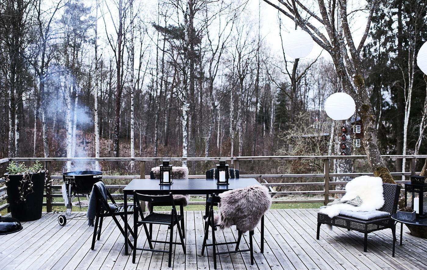 Table à manger et chaises sur une terrasse en bois avec barbecue allumé dans le fond