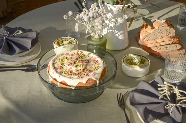Table avec gâteau, dips, pain, verres d’eau, couverts, serviettes et vases avec fleurs séchées et eucalyptus.