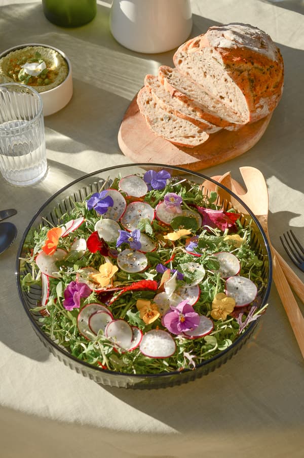 Table avec salade, pain, eau et dip aux herbes, couverts en bois et métal sur nappe claire.