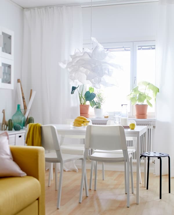 Table de salle à manger et chaises blanches près d’une fenêtre, avec suspension en papier de forme organique au-dessus.