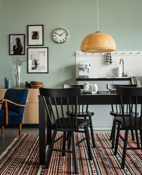 Table de salle à manger et chaises noires disposées dans un espace ouvert, entre la cuisine et le séjour.