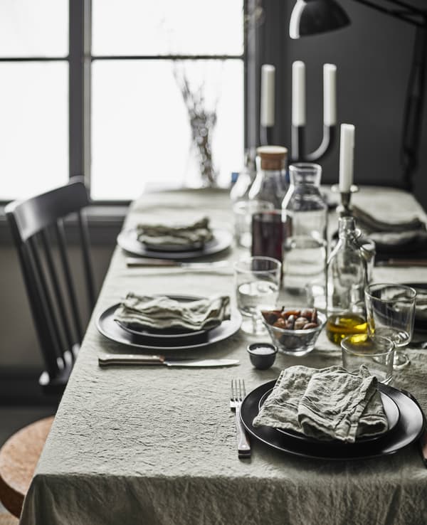 Table de salle à manger rustique et moderne, avec nappe en lin, sièges dépareillés et vaisselle moderne.
