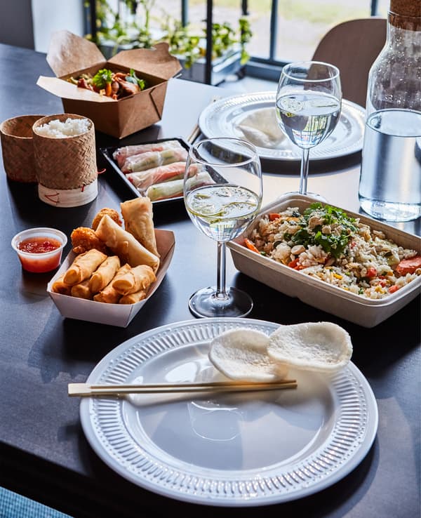 Table dressée avec verres à vin, vaisselle et plats à emporter asiatiques.