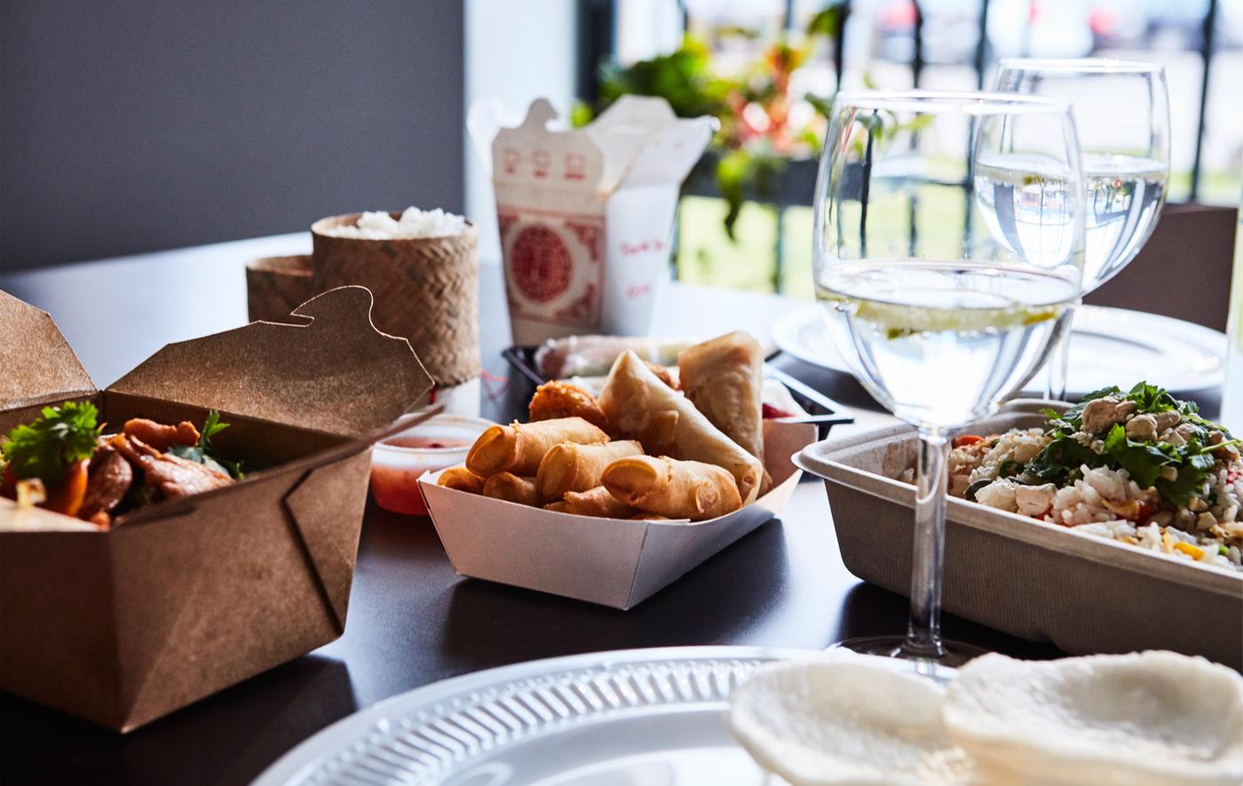 Table dressée avec verres à vin, vaisselle et plats à emporter asiatiques.